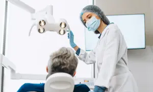 Dentystka w masce i rękawiczkach przygotowuje się do zabiegu. Pacjent siedzi na fotelu. Czy dentysta może wystawić L4?