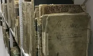 Des registres anciens, certains marqués "archive 07", s'alignent sur des étagères métalliques, témoins silencieux du temps.