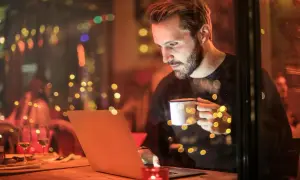Mężczyzna z kubkiem kawy pracuje na laptopie, szukając informacji o tym, jaki internet do domu bez światłowodu będzie najlepszy.