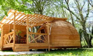 Cabane en bois et dôme de glamping Paca, avec terrasse et table extérieure, dans un cadre verdoyant.