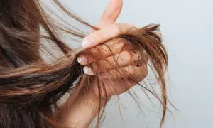 Mano che mostra capelli con doppie punte, un segno di capelli secchi e danneggiati che necessitano di cure.