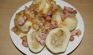 Pyszne pyzy z mięsem, okraszone skwarkami i cebulką, prezentują się apetycznie na białym talerzu.