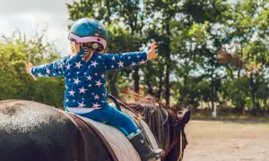 Mała dziewczynka w kasku i bluzie w gwiazdki cieszy się jazdą konną dla dzieci. Jej ramiona są szeroko rozłożone, jakby chciała objąć świat.