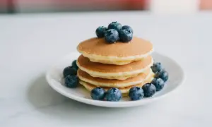 Stos puszystych pancakes z borówkami, ozdobiony świeżymi owocami. Idealne na słodkie śniadanie.