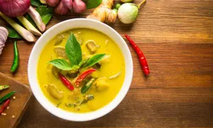 Aromaticzne curry z tofu, podane w białej misce, otoczone świeżymi składnikami: chili, trawą cytrynową, imbirem i cebulą.