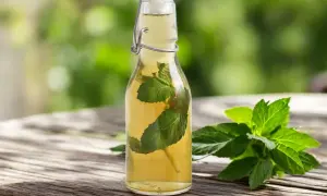 Bouteille de sirop de menthe maison avec des feuilles de menthe fraîche sur une table en bois.