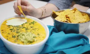 Salsa de queso cremosa con guacamole y nachos, una persona moja un totopo.