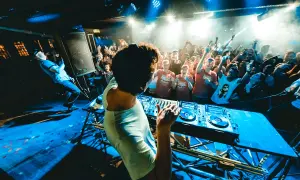 DJ na scenie, tłum szaleje w rytm drum and bass. Niebieskie światła, dym i energia.