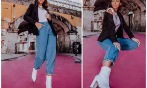 Kobieta w spodniach mom fit, czarnej marynarce i białych kozaczkach na różowym tle. Idealne dla każdej kobiety ceniącej wygodę i styl.