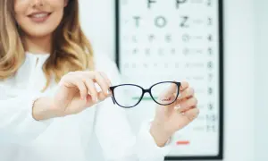 Kobieta trzyma okulary na tle tablicy Snellena.