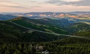 Długi, wiszący most w Czechach przecina gęsty las, łącząc dwa zbocza górskie. Widok zapiera dech w piersiach.