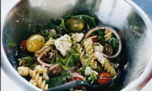 En härlig pastasallad vegetarisk med rotfrukter, oliver, fetaost och ruccola i en metallskål.