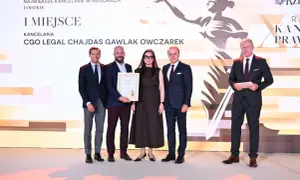 Cztery osoby w garniturach i sukience stoją na scenie, odbierając nagrodę.