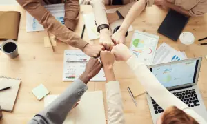 Equipo unido chocando puños sobre la mesa, simbolizando el logro de objetivos en la vida y metas compartidas.
