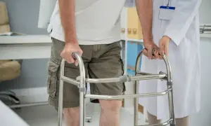 Un uomo con un deambulatore, aiutato da un medico, sta imparando a camminare di nuovo. Non riesco a camminare senza supporto.