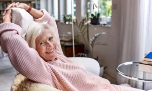 Vrolijke oudere vrouw ontspant in een fauteuil, genietend van rust. Een lat relatie elkaar weinig zien, maar ze vindt geluk in haar eigen gezelschap.