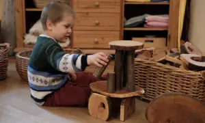 Ein Junge spielt mit Holzbausteinen, die das Waldorf Konzept widerspiegeln. Natürliche Materialien fördern Kreativität und Fantasie.
