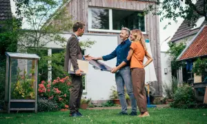 Beratung zu energetischer Sanierung Pflicht 2030: Ein Berater zeigt einem Paar ein Solarpanel im Garten vor ihrem Haus.
