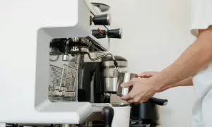 Barista spienia mleko w dzbanku, używając dyszy ekspresu. W tle widoczny blok zaparzający.