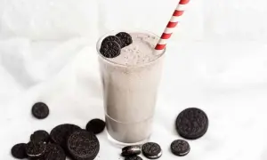 Batido cremoso de Oreo en un vaso con pajita a rayas, rodeado de galletas Oreo.