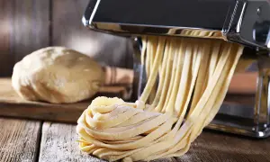 Świeży makaron wychodzi z maszynki, obok kulka ciasta. Idealny przepis na makaron domowy.