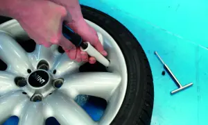 Ręce dokonują wymiany wentyla w oponie Mini. Narzędzie do wykręcania i nowy wentyl leżą obok.