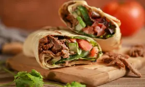 Kebab zawinięty w tortillę z mięsem, warzywami i ziołami na desce.
