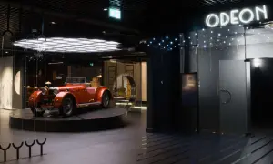 Pomarańczowy kabriolet z lat 20. XX wieku, symbol sztuki dwudziestolecia międzywojennego, prezentowany w nowoczesnym wnętrzu z neonowym napisem "ODEON".