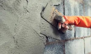 Mano con guanto arancione stende intonaco su muro di blocchi di cemento, mostrando la differenza tra geolite 10 e geolite 40.