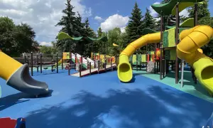 Kolorowy plac zabaw z żółtymi zjeżdżalniami i niebieską nawierzchnią.