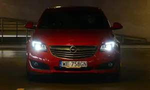Czerwony Opel z włączonymi światłami, gotowy do jazdy. Dowiedz się, jak ustawić światła w samochodzie domowym sposobem, by zapewnić sobie bezpieczeństwo.