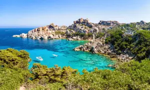 Türkisblaues Meer, Felsenbuchten und grüne Macchia – diese Szenerie verspricht die beste Reisezeit Sardinien. Kleine Boote schaukeln im Wasser.