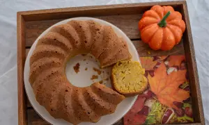 Un delicioso bizcocho de calabaza, con una porción cortada, sobre una bandeja de madera junto a una calabaza decorativa y una servilleta de hojas de otoño.