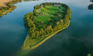 Wielkopolskie miasto koło Kalisza, Ostrowo Lednickie, z wyspą na jeziorze, porośniętą drzewami i trawą, z zabudowaniami.
