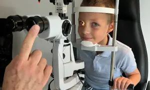 Chłopiec przechodzi badanie autorefraktometrii. Okulista bada jego wzrok za pomocą specjalistycznego sprzętu.
