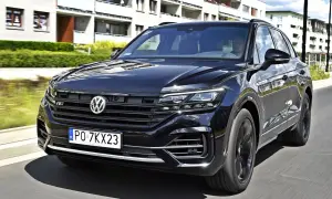 Czarny VW Touareg 3.0 TDI z polskimi tablicami PO 7KX23 jedzie ulicą obok nowoczesnych budynków.