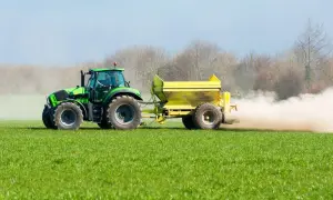 Tractor verde esparciendo cal viva en la huerta, creando una nube de polvo sobre el campo verde.