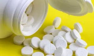 En vit burk med tabletter som kan vara adhd medicin för barn. Tabletterna ligger utspridda på en gul bakgrund.