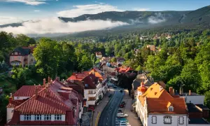 Widok na rynek w Szklarskiej Porębie z górami w tle. Urokliwe kamienice z czerwonymi dachami i zielone drzewa tworzą malowniczy krajobraz.