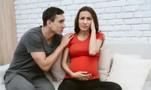 Uomo consola donna incinta con mal di testa, preoccupati per la crisi di coppia in gravidanza.