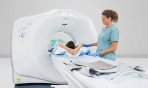 Pacjent leży na stole tomografu, pielęgniarka w rękawiczkach przygotowuje badanie PET.