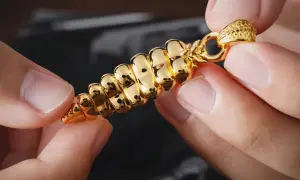 Manos sostienen un colgante dorado brillante, con forma de espiga. ¿Cómo saber si es oro? Su brillo intenso y diseño detallado sugieren autenticidad.