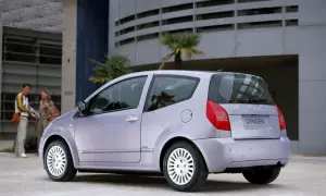 Jasnoszary Citroën C2 z parą stojącą w tle przed nowoczesnym budynkiem.