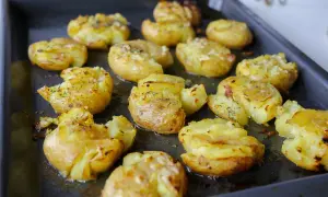 Ugnsbakade smashed potatoes med ost och örter på en plåt. Krispiga och gyllene, redo att serveras.