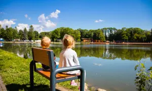 Dwoje dzieci siedzi na ławce, patrząc na spokojny zalew nowohucki.