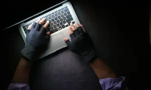 Ręce w rękawiczkach bez palców piszą na laptopie, szukając informacji, co może prowadzić do doxxingu.