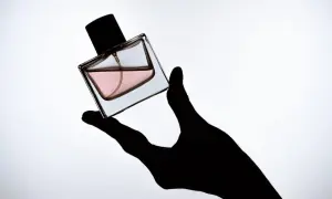 Czarna dłoń trzyma flakonik perfum z różowym płynem. To Twój **signature scent**, który podkreśla Twój styl.