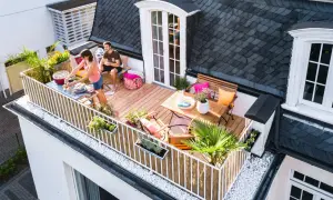 Ein Paar genießt den Sommer auf einem gemütlichen Balkon mit Grill und Sitzgelegenheiten. Tolle Balkon Ideen für entspannte Stunden.