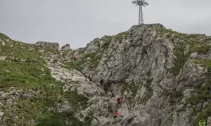 Grupa turystów wspina się po kamienistym szlaku na Giewont. W oddali widać charakterystyczny krzyż.
