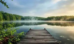Drewniany pomost nad spokojnym jeziorem kacze oko, otoczonym lasem. Poranna mgła unosi się nad wodą, tworząc magiczną atmosferę.